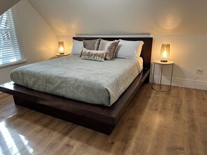 A bedroom with a large bed, two bedside lamps, and a window with blinds. - Quaint 3-bedroom Cottage in Logan Utah (Logan)