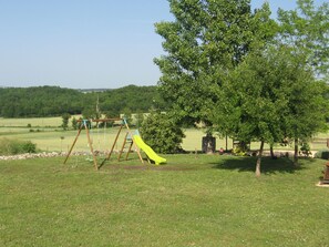 A playground with a swing set and a slide in a grassy field with trees and a clear sky. - New Listing (Villeréal)
