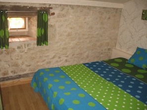 A bedroom with a stone wall, a window with curtains, and a bed with polka dot bedding. - New Listing (Villeréal)
