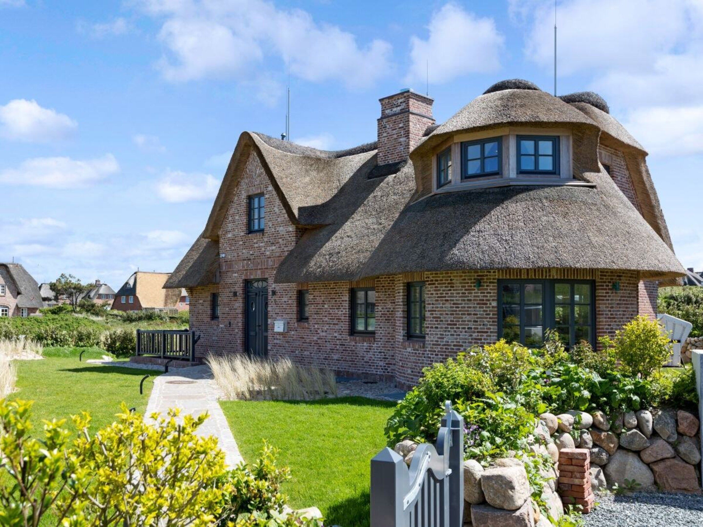 A traditional thatched-roof house with a brick exterior, a visible chimney, and a well-maintained garden with a pathway leading to the entrance.