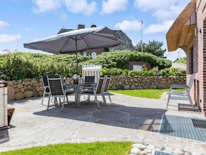 An outdoor patio with a table and chairs, a large umbrella, and a stone wall. - Holiday Home in Rantum With Swimming Pool (Sylt)