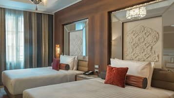 A hotel room with two beds, a large mirror, and a modern chandelier.