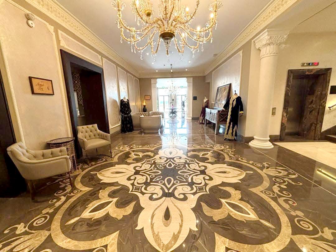 Un amplio pasillo con candelabro, suelo estampado y vista a una habitación con bañera.