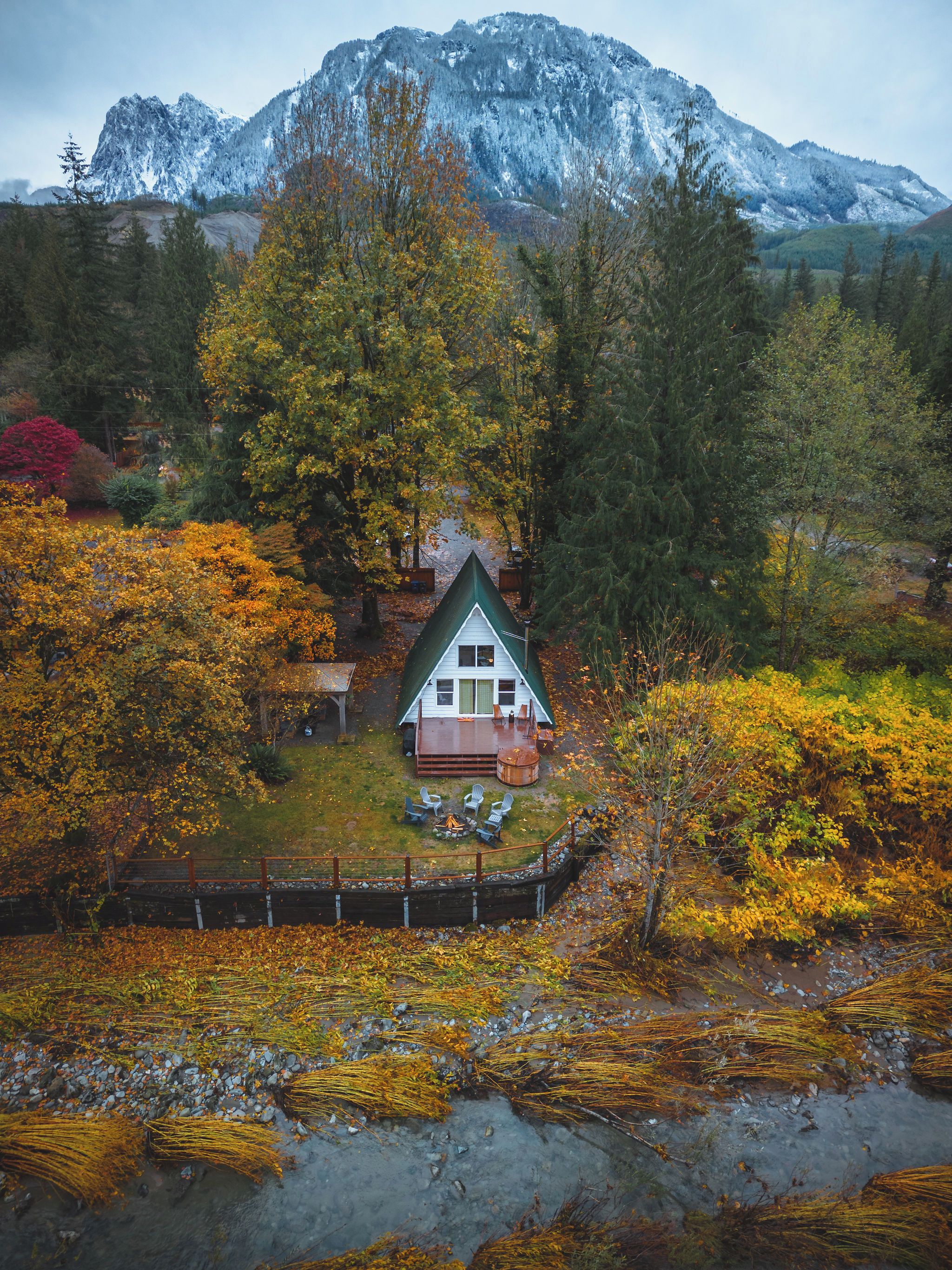 A cabin with a deck, surrounded by autumn foliage, with a mountain in the background.