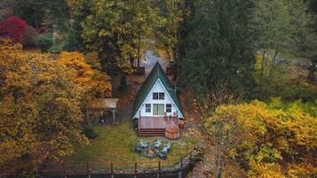 A cabin with a deck, surrounded by autumn foliage, with a mountain in the background.