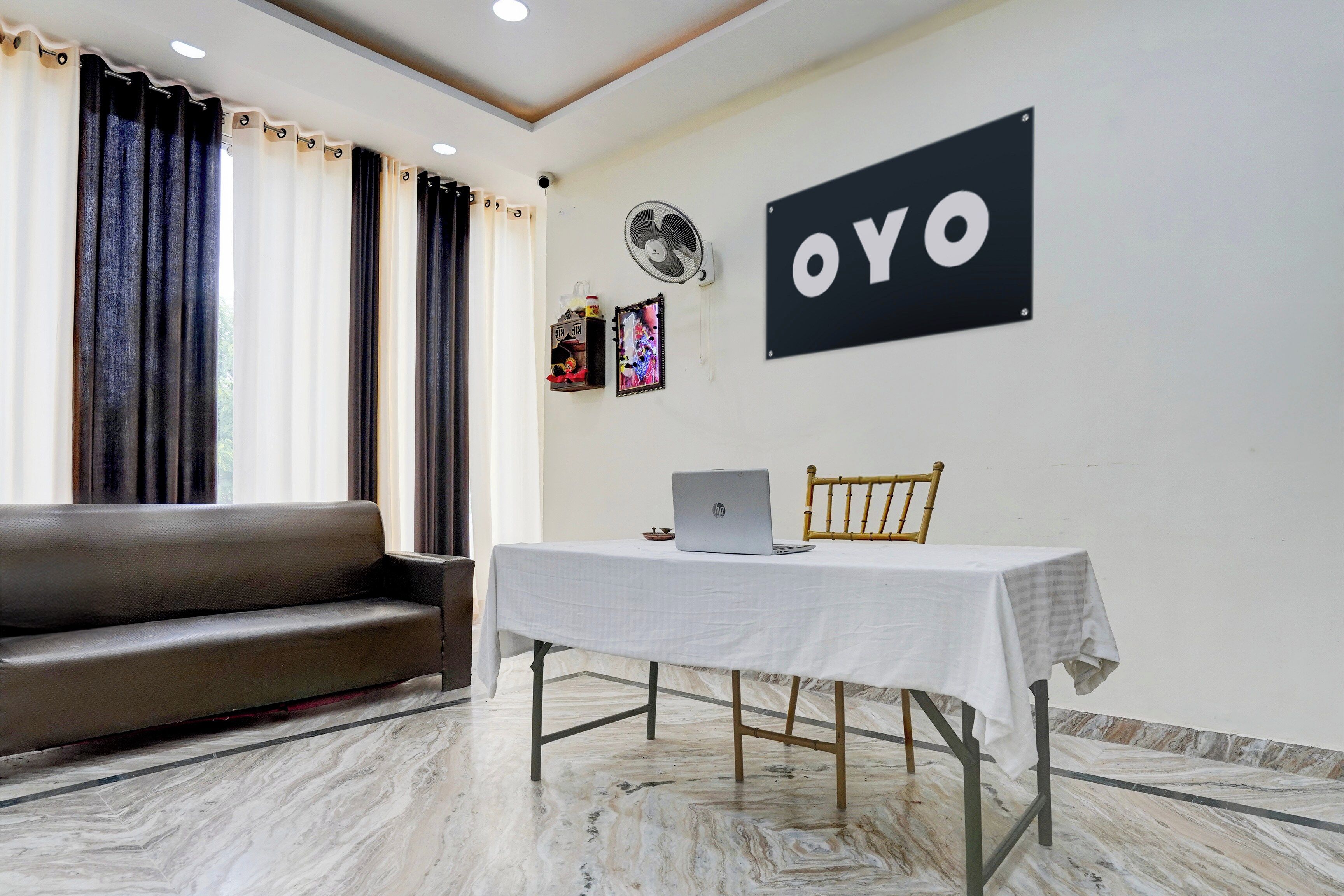 A room with a sofa, a table with a laptop, a fan, and a sign on the wall.