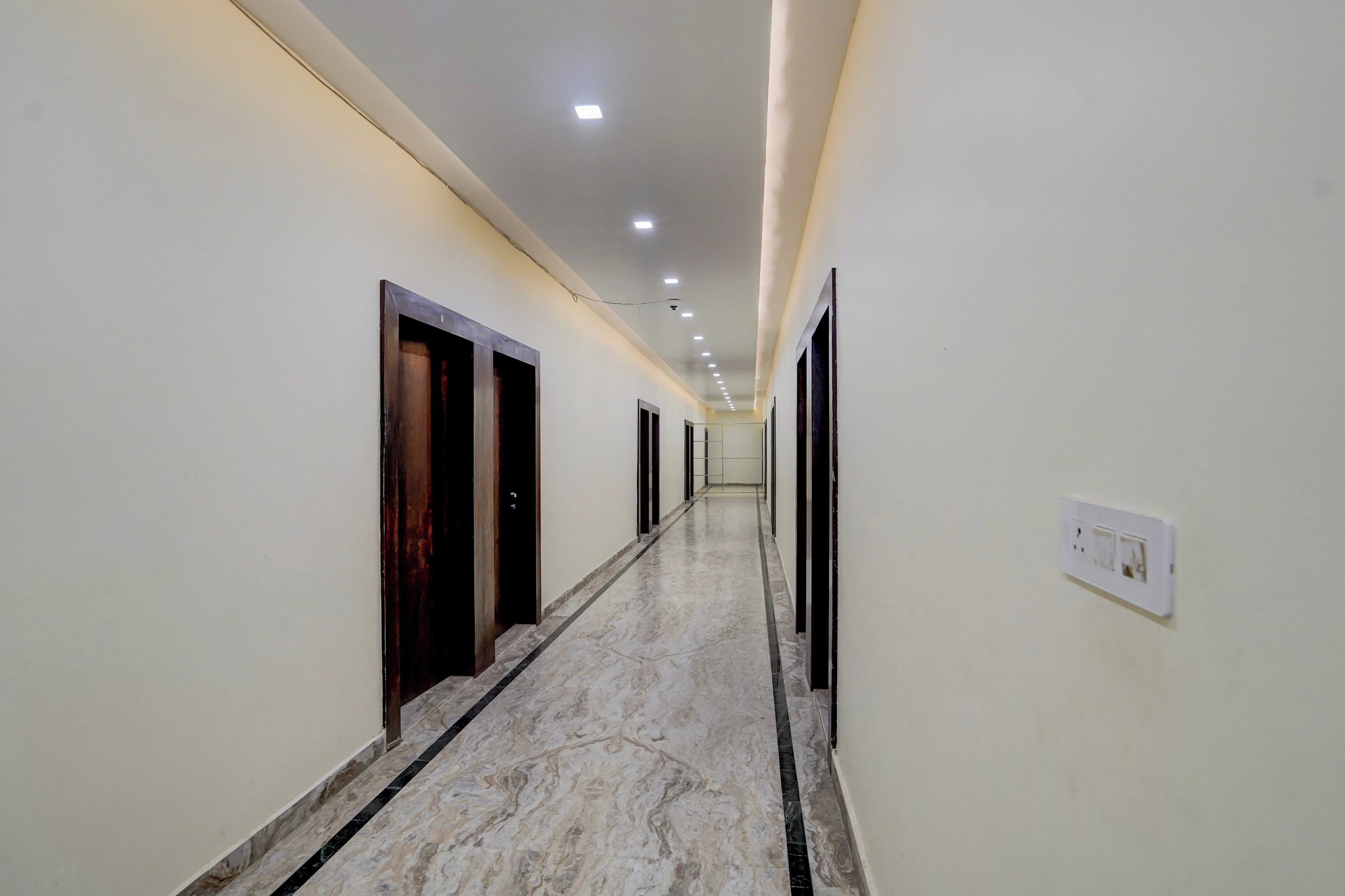 A hallway with a marble floor, doors on both sides, and recessed lighting.