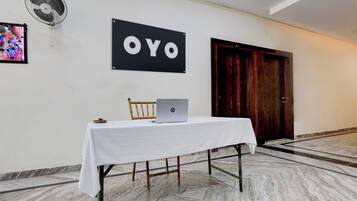 A hotel room with a white table, a laptop, a fan, and a door.