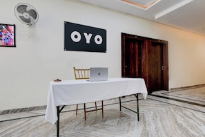 Una habitación de hotel con una mesa blanca, una computadora portátil, un ventilador y una puerta.