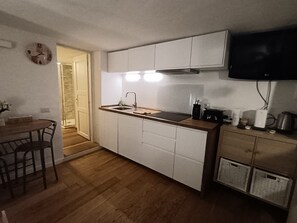 A compact kitchen with white cabinets, a wooden countertop, a built-in stove, and a television mounted on the wall. - New Listing (Porto rotondo)