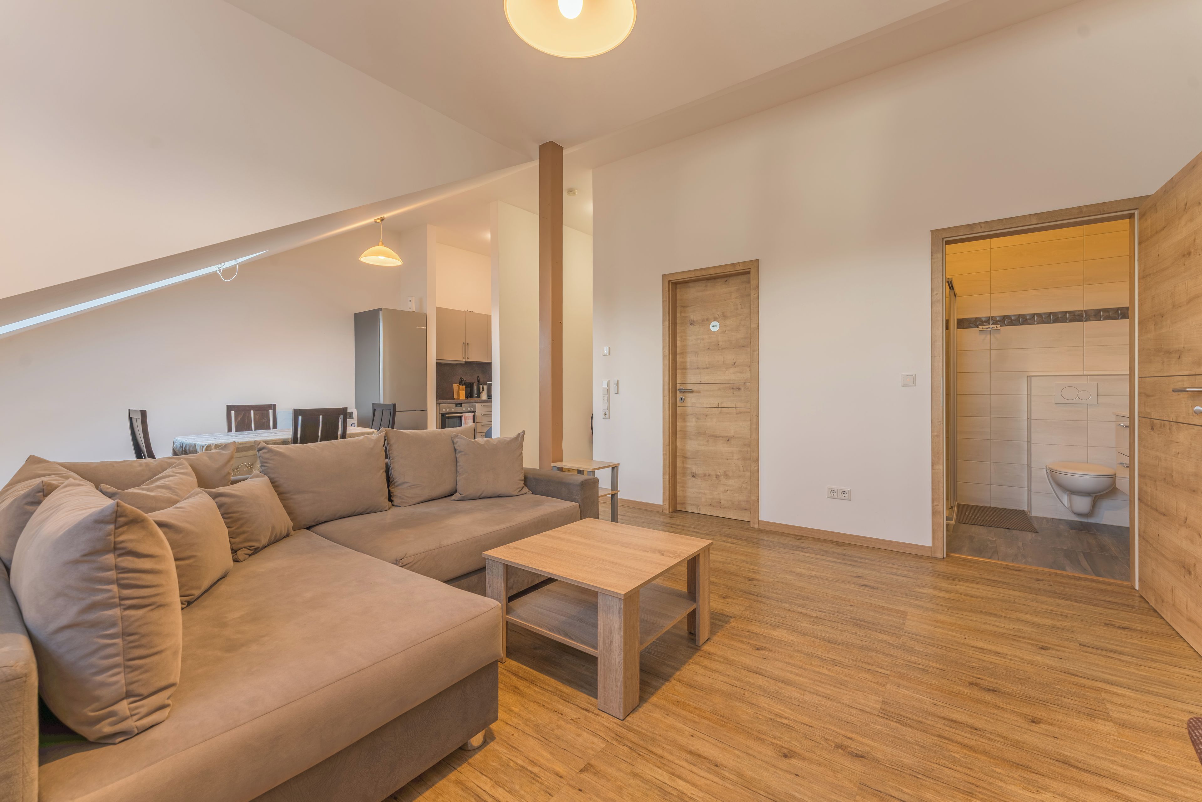 A modern living room with a sectional sofa, a wooden coffee table, and a kitchen in the background.