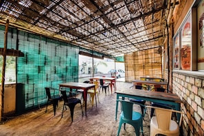 Un espace extérieur aménagé avec des tables et des chaises, un plafond en bambou et une vue sur la rue.