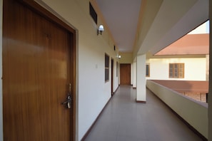 A corridor with a wooden door on the left, a light fixture on the wall, and a window on the right. - Hotel O Anand Hotel Jodhpur (Jodhpur)