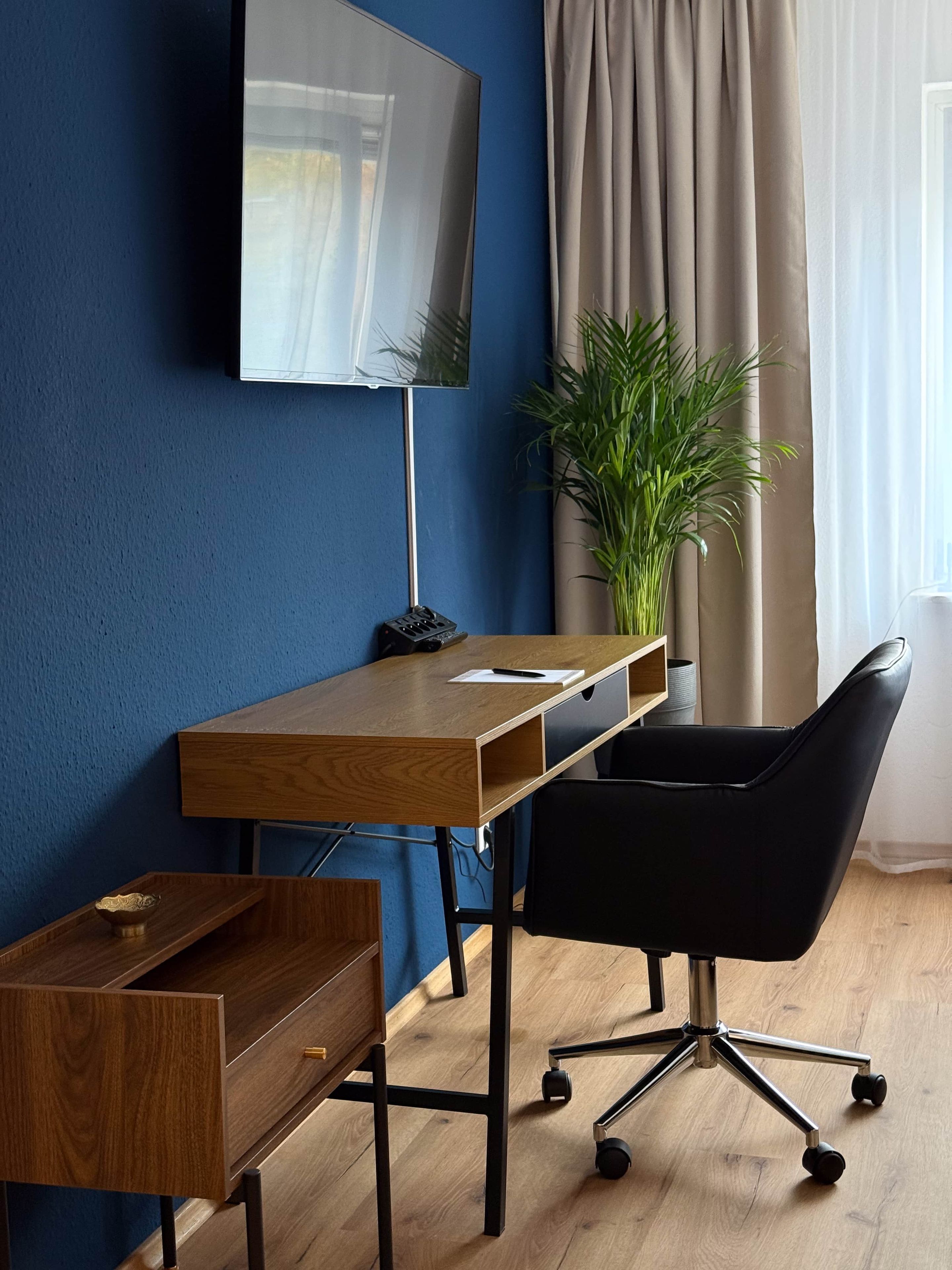 Ein moderner Arbeitsbereich mit einem Holztisch, einem schwarzen Bürostuhl und einem an der Wand befestigten Fernseher.