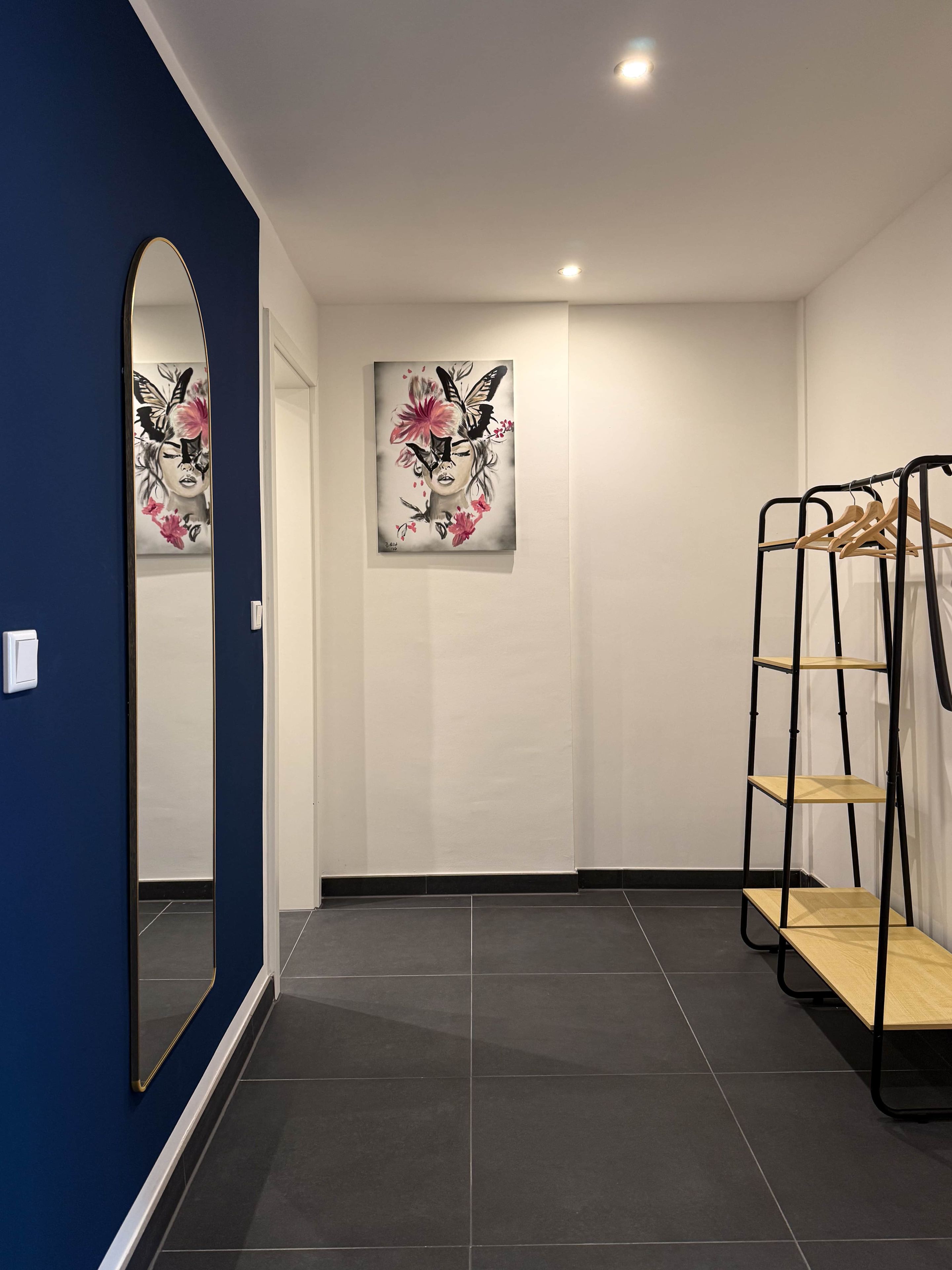 Ein Flur mit blauer Wand, einem Spiegel, einem Gemälde und einem Kleiderständer.
