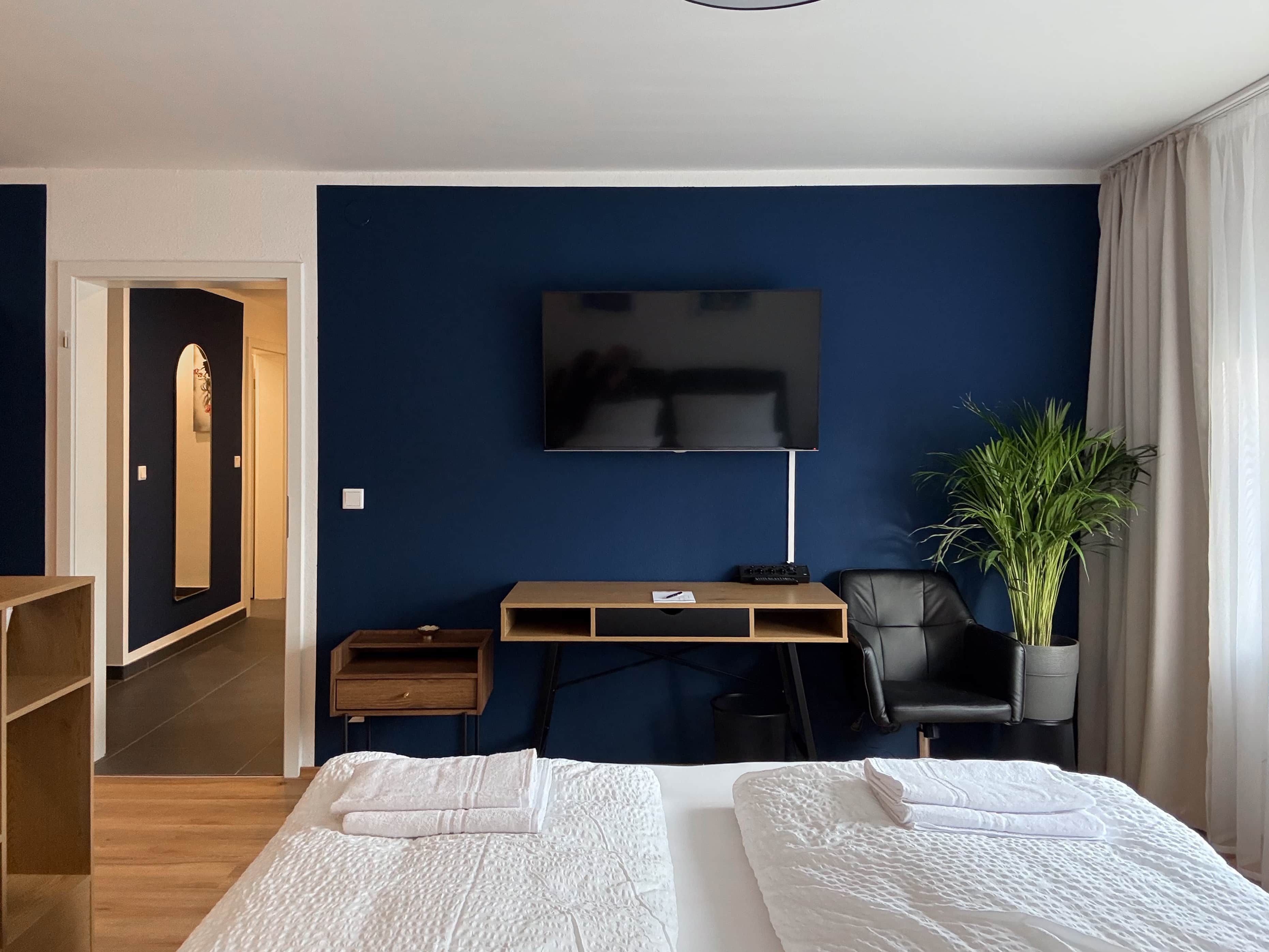 A hotel room with a bed, a desk, a chair, a television, and a potted plant.