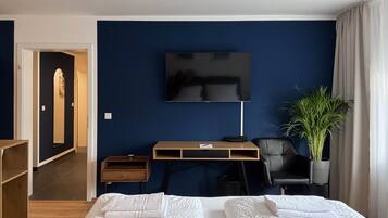 A hotel room with a bed, a desk, a chair, a television, and a potted plant.