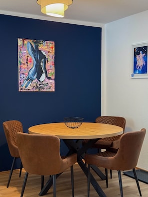 A dining area with a round wooden table, four brown chairs, and two wall-mounted paintings. - Nexpo Executive, Luxury Apartment + Free Parking (Nürnberg)