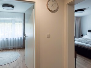 A hotel room with a bed, a round wall clock, a door, and a view of a window with curtains.