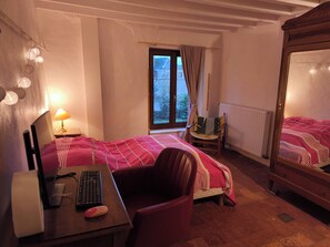 Un dormitori amb un llit, un escriptori amb un ordinador, una cadira i una finestra amb cortines.