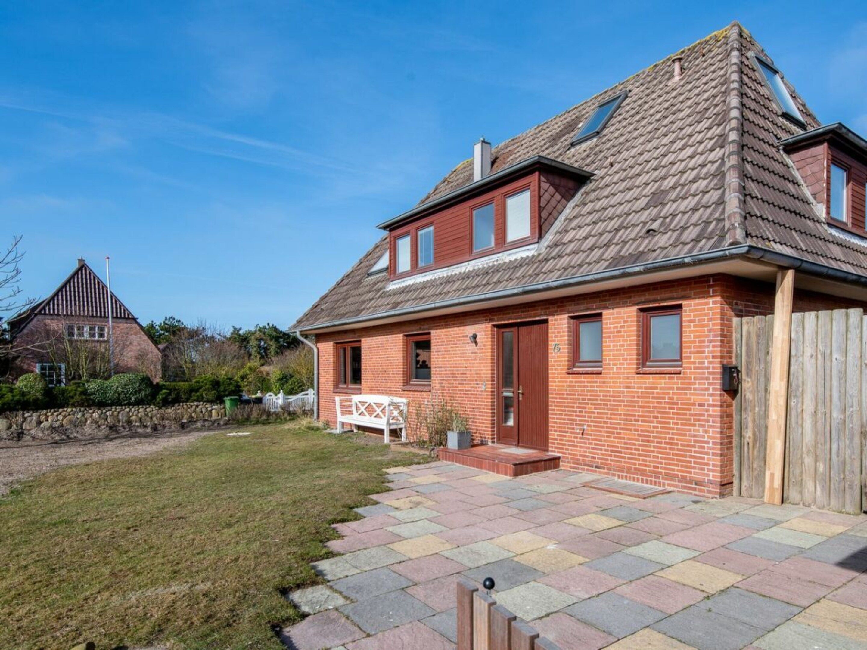 A two-story house with a tiled patio, a wooden fence, and a stone wall.