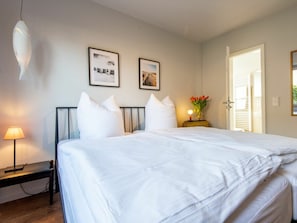 Ein Schlafzimmer mit einem Bett, Kissen, einem Nachttisch mit Lampe, einem Beistelltisch mit Blumen und zwei gerahmten Bildern an der Wand.