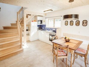 A kitchen with a wooden staircase, a dining table with chairs, and a tiled floor. - Luna Blanca Chalet (Schwangau)
