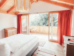 A bedroom with a bed, a wooden dresser, a small table, and a balcony with chairs. - Luna Blanca Chalet (Schwangau)