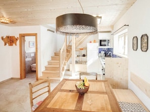 A wooden dining table with a bowl of fruit, a staircase leading to a kitchen, and a ceiling light fixture. - Luna Blanca Chalet (Schwangau)