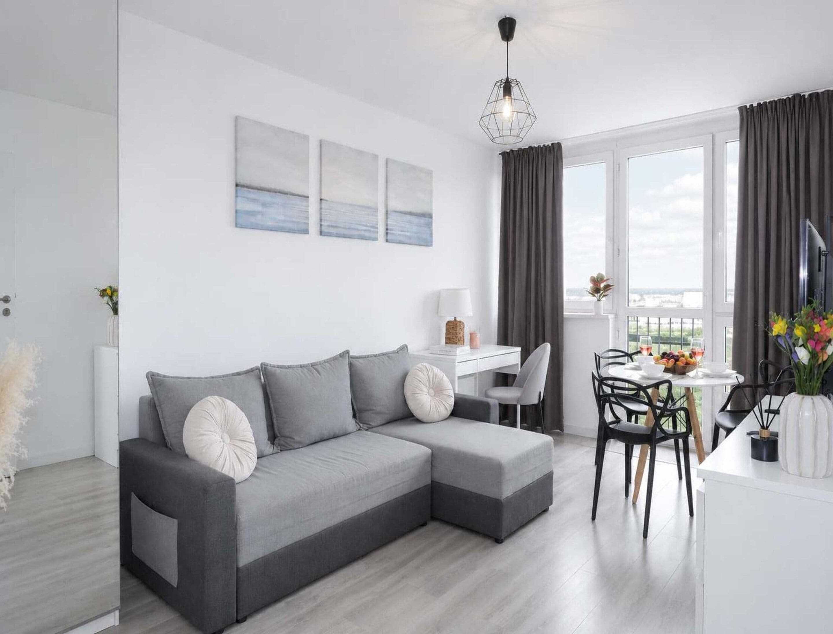 Una sala moderna con un sofá seccional gris, un escritorio blanco y un comedor con sillas.