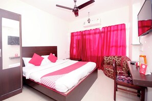 Une chambre d’hôtel avec un lit, une chaise, un bureau, un ventilateur de plafond et une fenêtre avec des rideaux.