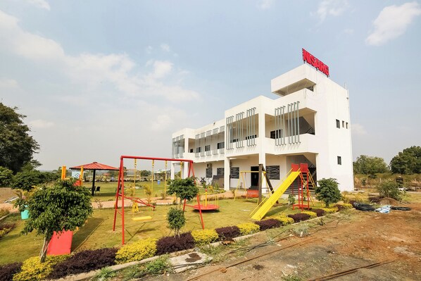 A modern building with a playground in front, including swings and a slide.