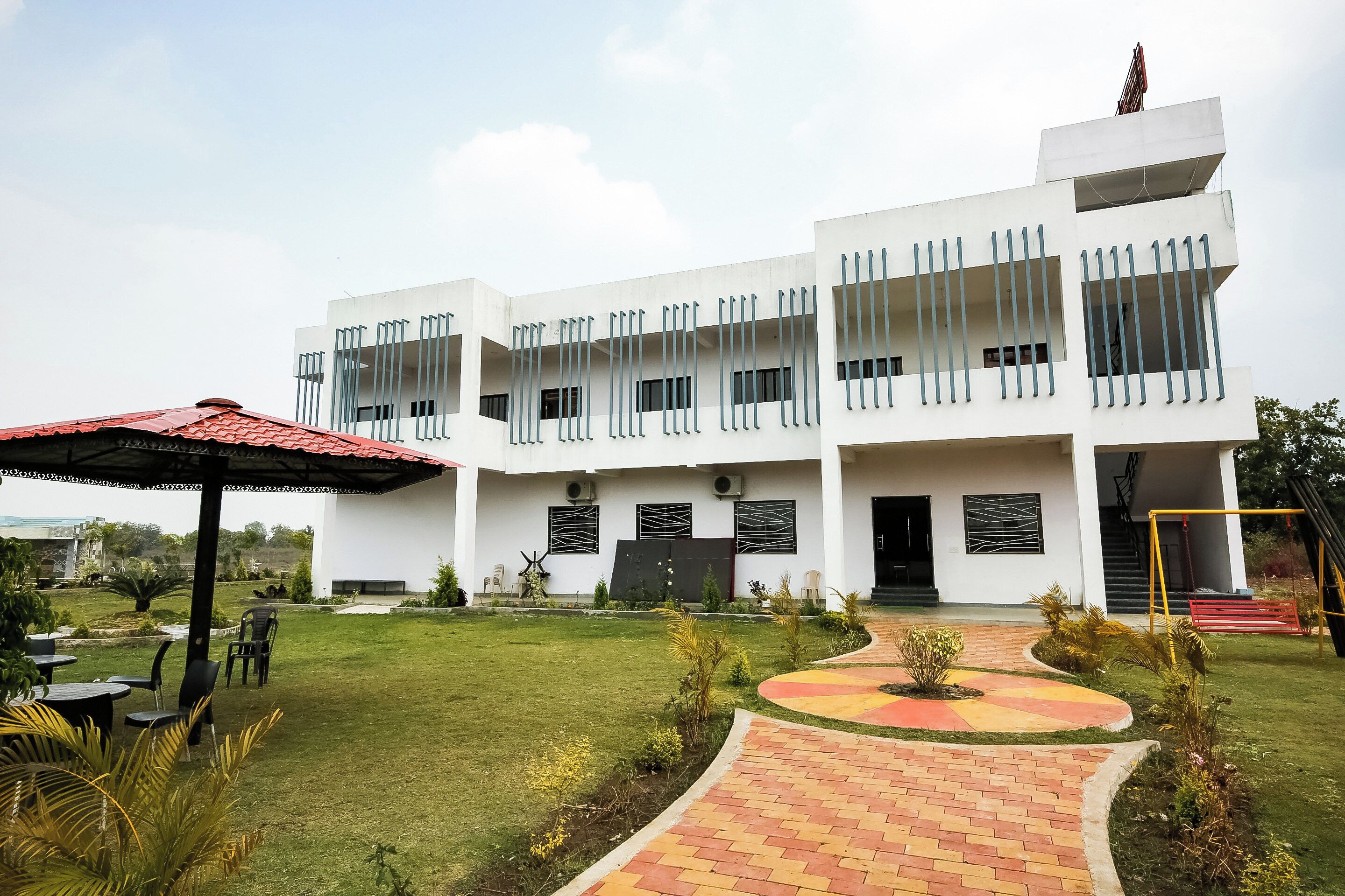 A modern building with a flat roof, multiple balconies, and a paved walkway leading to the entrance.