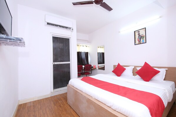 A hotel room with a bed, a ceiling fan, an air conditioning unit, a window, a mirror, and a wall-mounted artwork. - Hotel O Sukooon City View (Jabalpur)