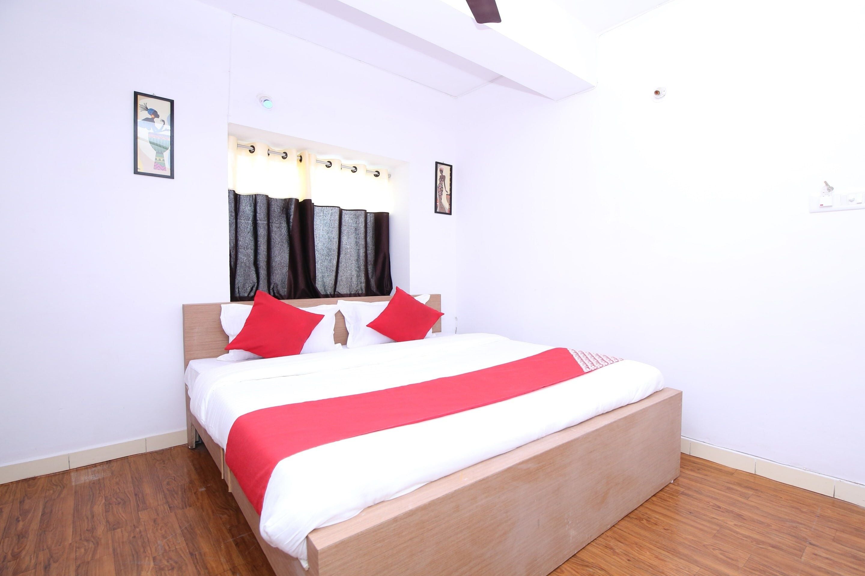 A bedroom with a wooden bed, white and red bedding, a window with curtains, and a wooden floor.