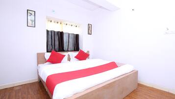 A bedroom with a wooden bed, white and red bedding, a window with curtains, and a wooden floor.