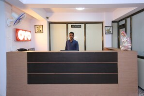 A reception desk with a sign reading 'RECEPTION' above it, a framed floral artwork on the wall, and a large illuminated sign with the number '070'. - Hotel O Sukooon City View (Jabalpur)