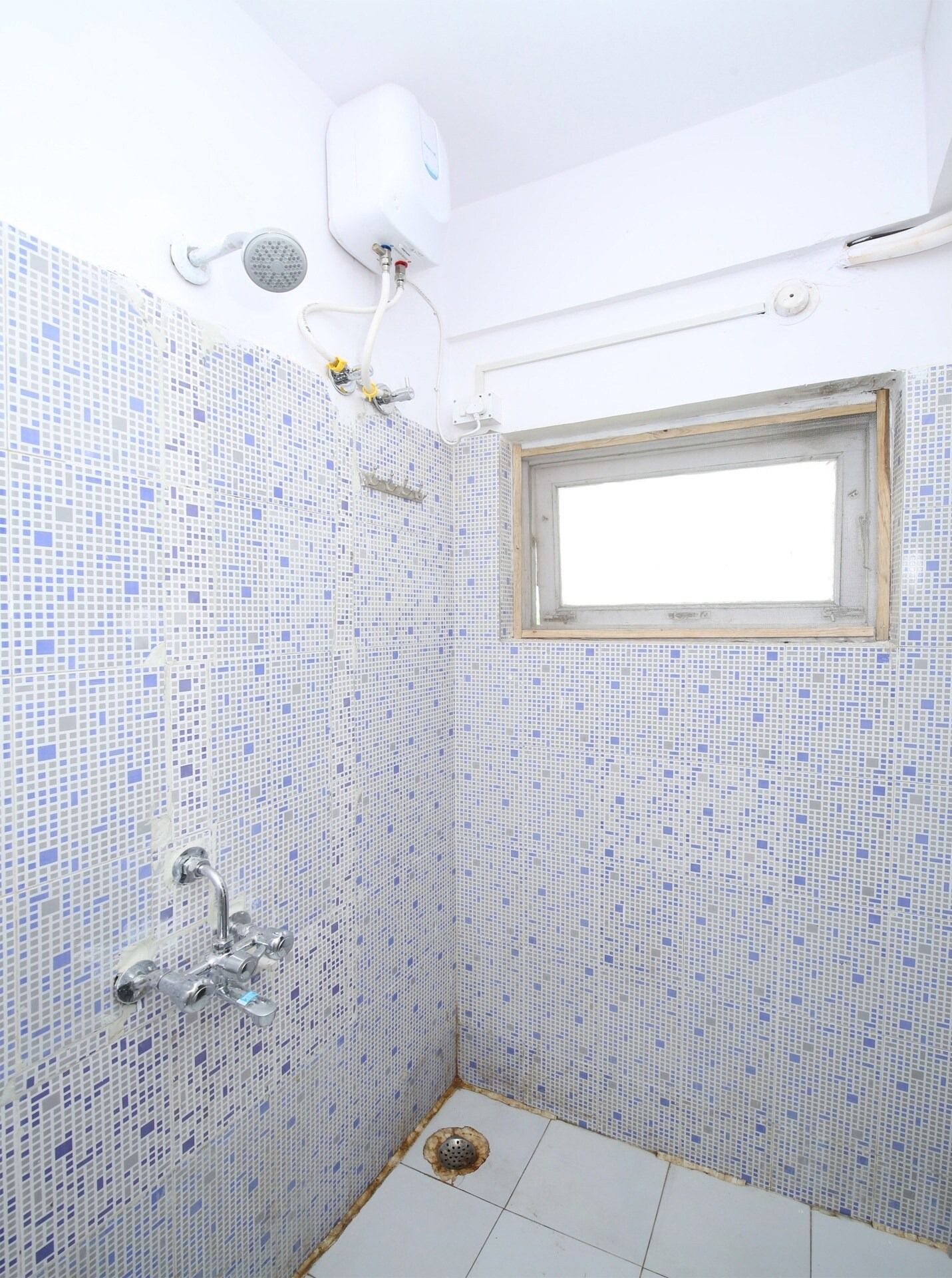 A small bathroom with a shower, a window, and a tiled floor.