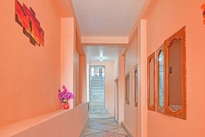 Un pasillo con una escalera que sube a un piso superior, un jarrón con flores a la izquierda y un espejo a la derecha.