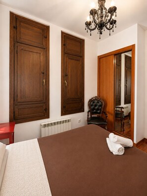 Un dormitorio con una cama grande, un armario de madera, un radiador, una silla y una araña.