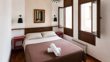 Quarto de hotel com cama, mesa de cabeceira, espelho, lustre e janela com persianas.