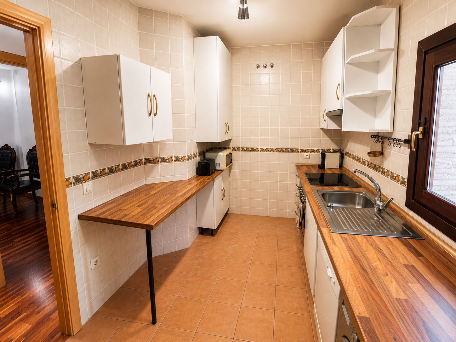 Una cocina compacta con armarios blancos, encimera de madera y un lavamanos empotrado.