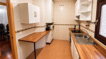 Una cocina compacta con armarios blancos, encimera de madera y un lavamanos empotrado.