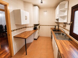 Una cocina compacta con armarios blancos, encimera de madera y un lavamanos empotrado.