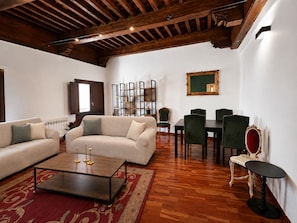 Una sala de estar amplia con techo de madera, un conjunto de sofá, una mesa de comedor con sillas y una pequeña mesita auxiliar.