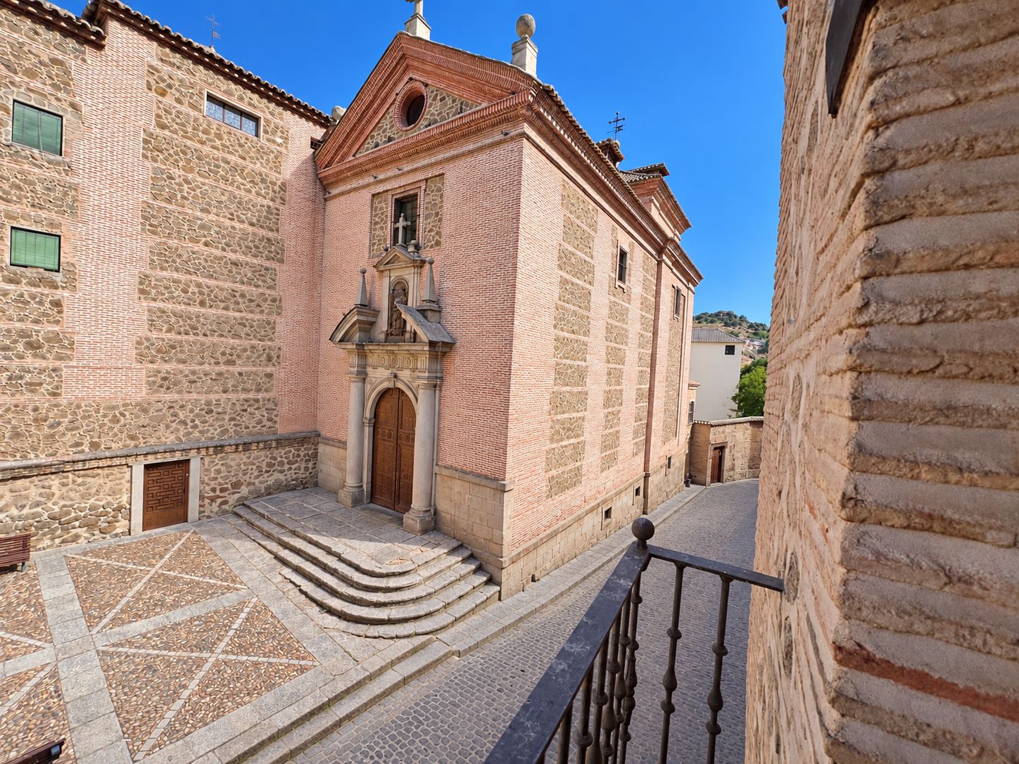 A narrow street with a stone building featuring a wooden door and a small staircase leading to a door.