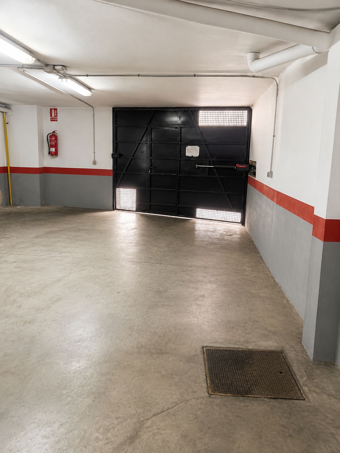 A parking garage with a concrete floor, a fire extinguisher mounted on the wall, and a fire hose.