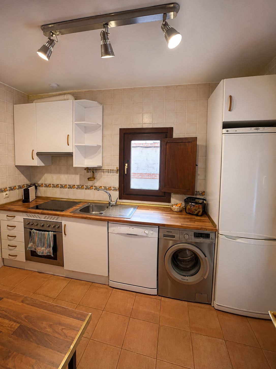 Una cocina compacta con armarios blancos, horno empotrado, lavavajillas, lavadora y refrigerador.