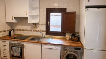 Una cocina compacta con armarios blancos, horno empotrado, lavavajillas, lavadora y refrigerador.