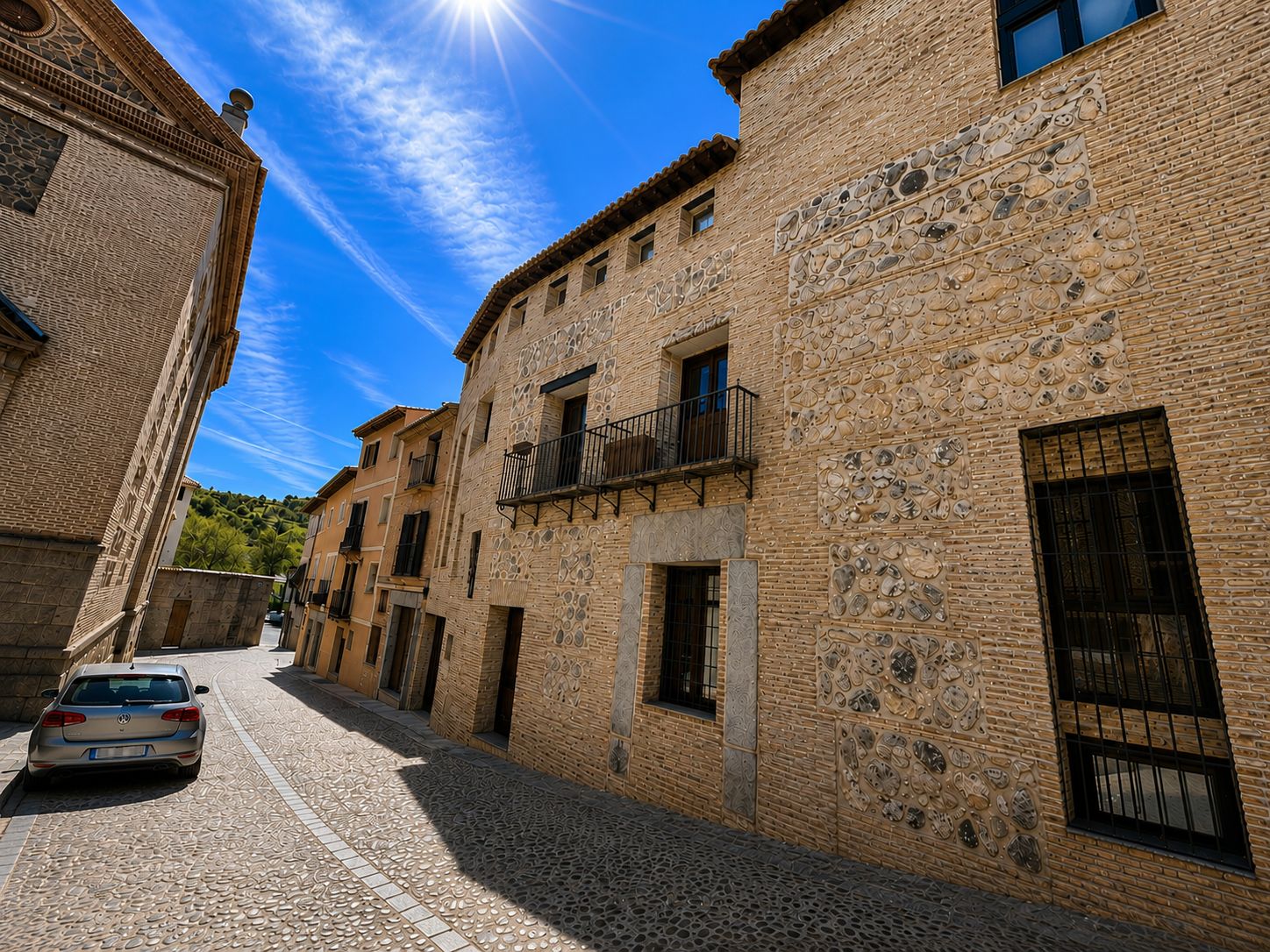 A narrow cobblestone street lined with traditional stone buildings, featuring balconies and windows.